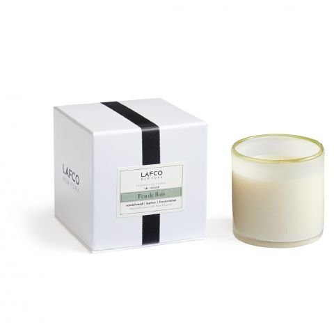 A glass candle with creamy wax sits beside a white LAFCO New York box featuring a black stripe and Feu De Bois label, highlighting notes of leather accord, sandalwood, and frankincense.