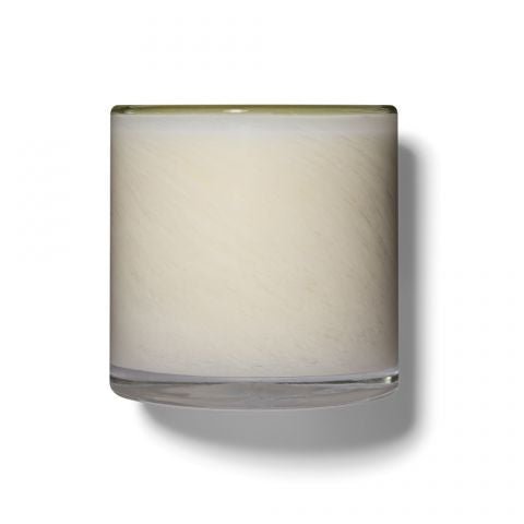 The Lafco - Feu De Bois Signature 15.5oz Candle features a minimalist design in a clear glass container. It embodies a sandalwood essence, with its cylindrical and smooth surface casting shadows on a white background.