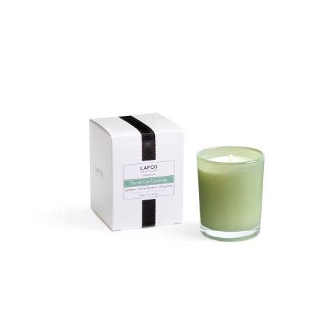 A green glass LAFCO votive candle with a white wick and a black ribbon-adorned white box sits against a plain backdrop. The label reads Fresh Cut Gardenia, capturing the essence of blooming gardenia.