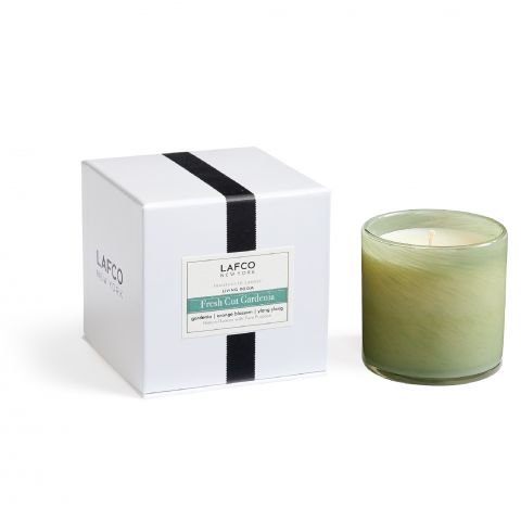 A green glass candle labeled Lafco - Fresh Cut Gardenia Classic 6.5 Candle sits beside its white box with black accents, both marked with the Lafco brand and scent. The packaging hints at orange blossom notes, while the unlit candle awaits to infuse your space with its fragrance.