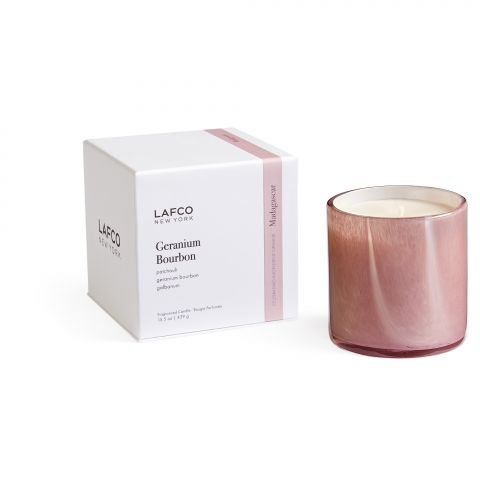 The Lafco - Geranium Bourbon Classic 15.5oz Candle, encased in pink glass, sits beside its matching pink and white packaging, infusing your space with a hint of Galbanum. The brand Lafco is prominently displayed on both the candle holder and its packaging.