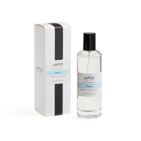 A clear bottle of Lafco - Marine Room Mist, a refreshing marine fragrance with a blue label, stands next to its white box packaging featuring a simple vertical black stripe and matching branding.