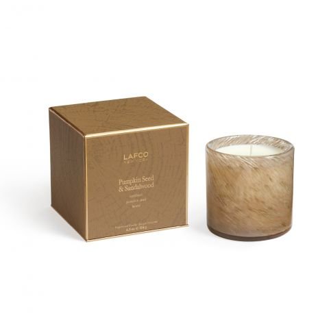 The Lafco - Pumpkin Seed & Sandalwood Signature 6.5oz Candle sits in a marbled beige glass jar next to its gold-brown box, highlighting warm pumpkin seed and sandalwood scents.