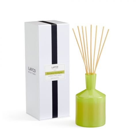 The Lafco Rosemary Eucalyptus 6oz Reed Diffuser, showcased in a green glass with natural sticks, releases rosemary and eucalyptus scents beside a tall white box featuring a black stripe and the brand Lafco New York.