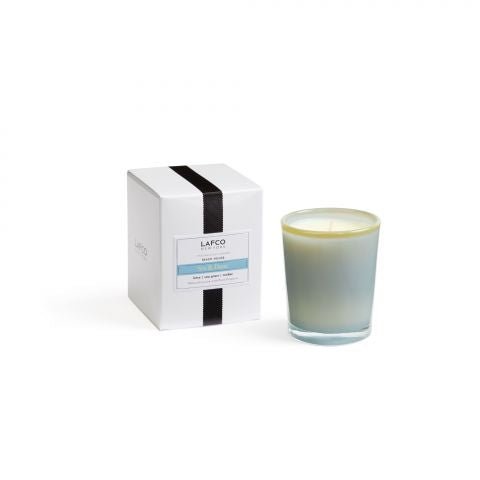 The Lafco - Sea & Dune 1.9oz Votive Candle, in a blue and white glass holder beside a box with a black stripe and the Lafco name, captures the beach house essence. Its serene scent won the Allure Best of Beauty Award.