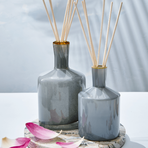 The Lafco - Sea & Dune 6oz Reed Diffuser from Lafco sits on a marble tray, with wooden reeds and scattered petals nearby, suggesting fresh blue lotus notes in the air beneath a soft light.