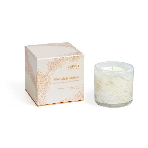 The Lafco White Maple Bourbon Signature 6.5oz Candle, in hand-blown glass with gold flecks, sits beside its matching cream box labeled "White Maple Bourbon" and decorated with subtle gold speckles and orange text.