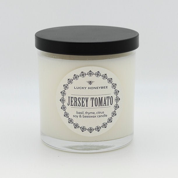 The Lucky Honeybee - Jersey Tomato Candle, in a glass jar with a black lid, captures the essence of Garden State tomatoes with basil, thyme, and citrus aromas. Made from soy and beeswax, it delivers an alluring fragrance.