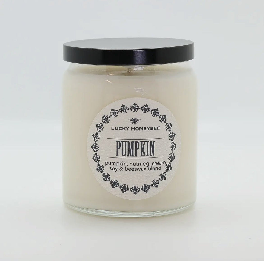 The Lucky Honeybee - Pumpkin Candle features a white jar with a black lid and branded label. This fall-scented soy beeswax blend combines pumpkin, nutmeg, and cream. Shown against a plain white background.