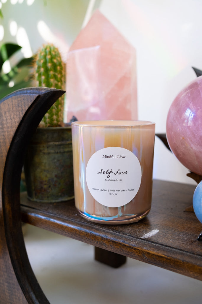 The Mindful Glow - Self Love Candle 13oz, crafted with coconut soy wax, graces a wooden shelf alongside a potted cactus and rose quartz crystals, creating a serene ambiance.