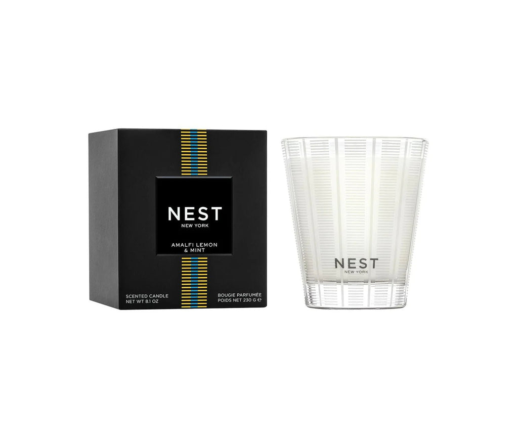 A Nest - Amalfi Lemon & Mint Classic Candle in a clear, white-striped glass sits beside its black box, both showing the Nest brand and product name. The candle is cruelty-free.