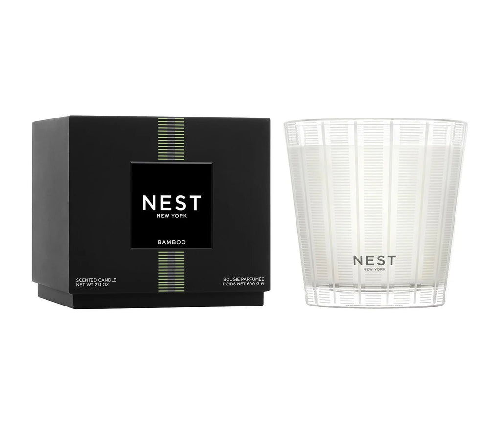 A black box labeled Nest - Bamboo 3-Wick Candle sits beside a white, striped glass holder, both featuring the Nest branding and offering a clean burn with a fresh bamboo fragrance.