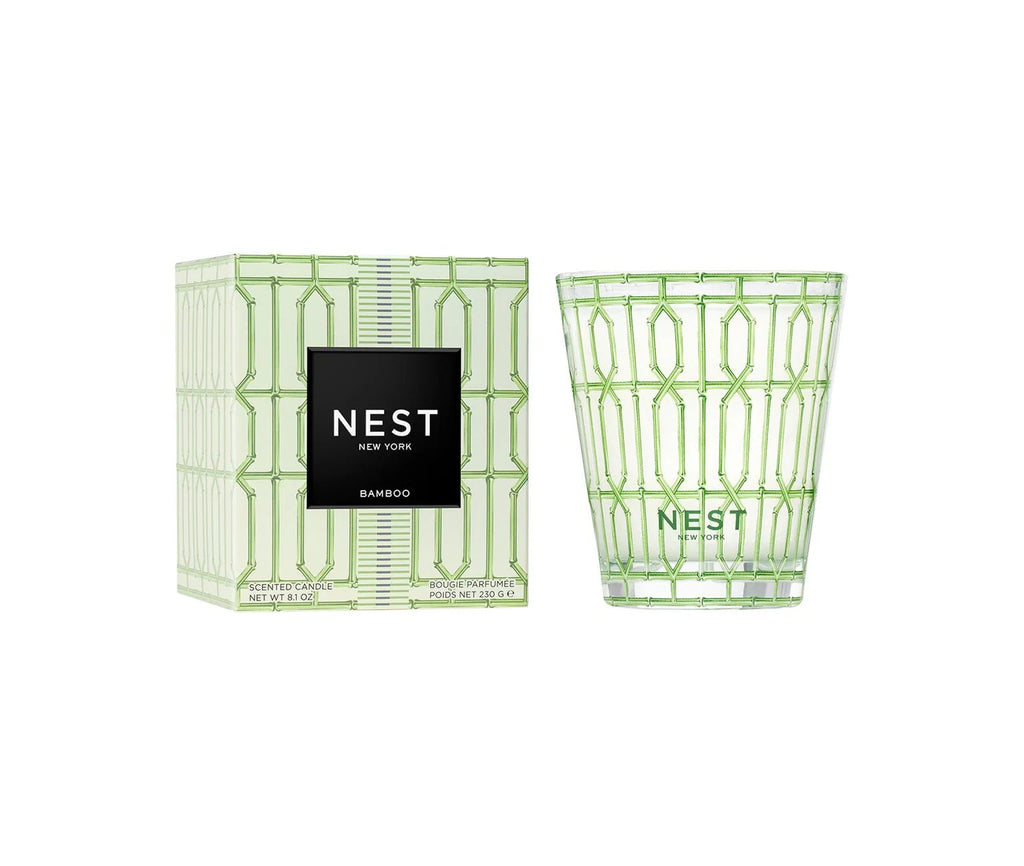 The Nest - Bamboo Decorative Classic Candle by Nest is displayed in a glass holder with a green geometric pattern beside its matching box, both branded with Nest and featuring a bamboo fragrance with floral notes.