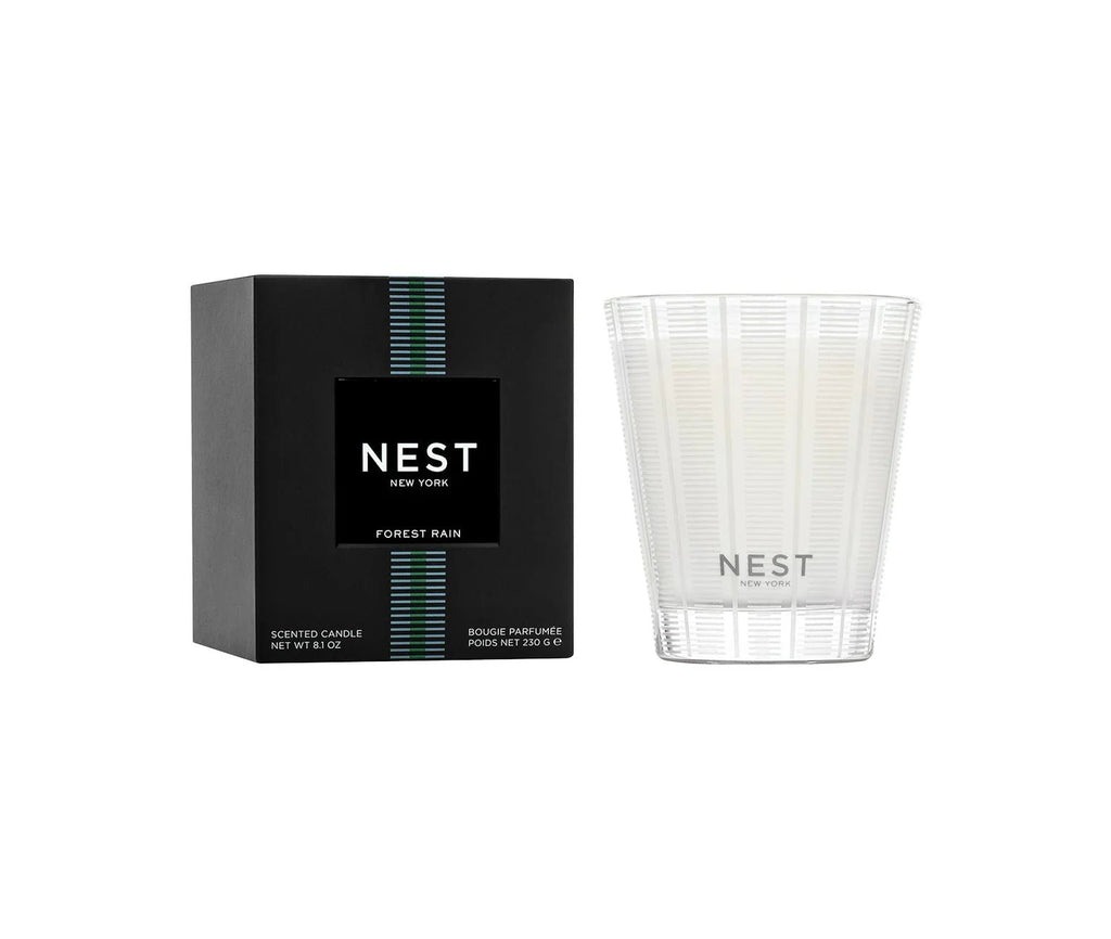 The Nest - Forest Rain Classic Candle features premium white scented wax in a striped glass holder. It comes in a black box with green and blue vertical lines above the Nest New York label.