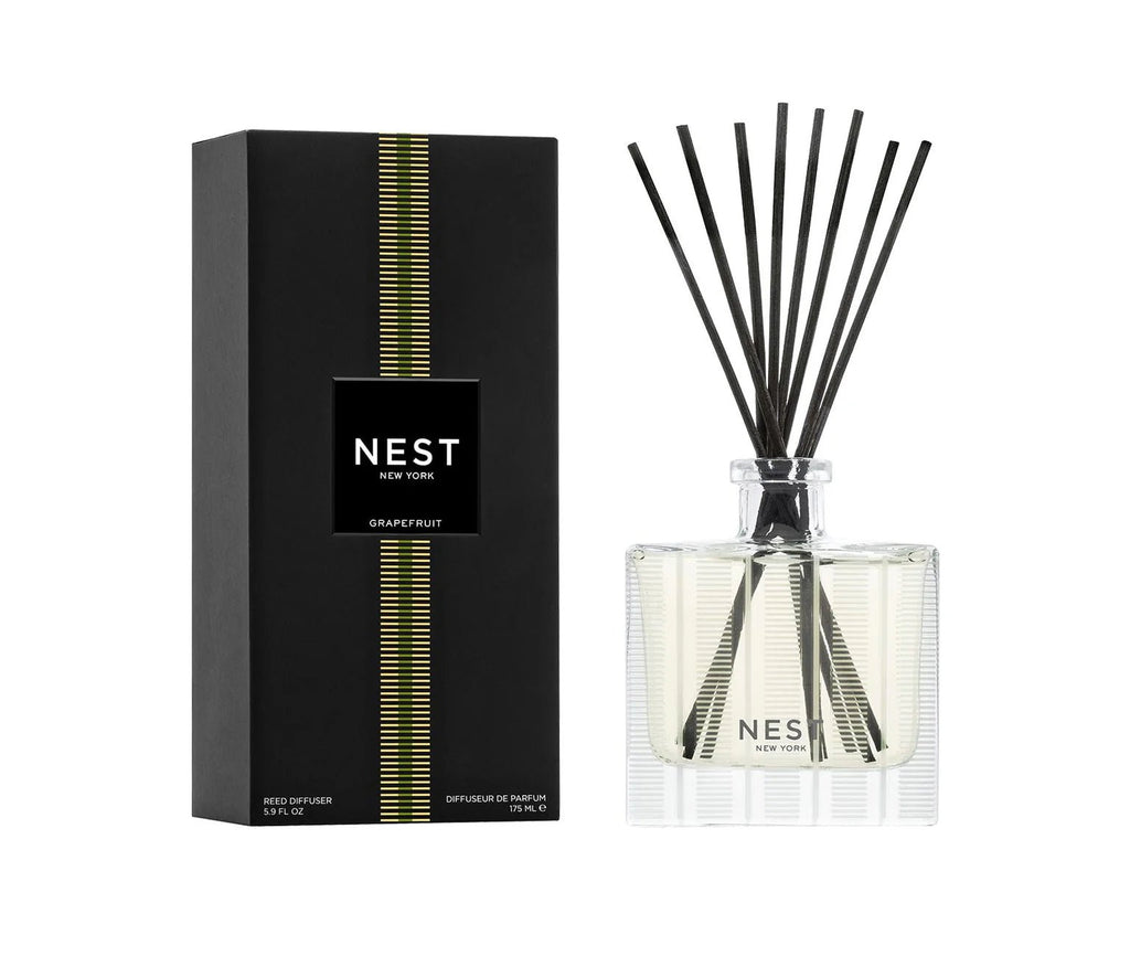 The Nest - Grapefruit Reed Diffuser by Nest features black reeds in a clear glass bottle and sleek black packaging with green stripes, releasing an invigorating citrus scent.