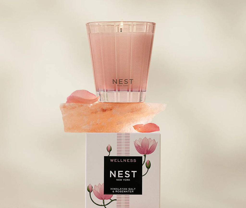 A Nest - Himalayan Salt & Rosewater Classic Candle in a patterned glass holder sits atop a Himalayan salt rock and rests on its floral Nest Wellness candle box.
