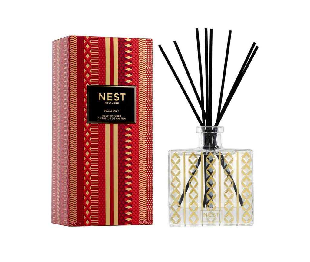 Discover the cruelty-free elegance of the Nest Holiday Reed Diffuser. Encased in red packaging with festive gold and white patterns, this clear glass bottle features a gold geometric design and black reed sticks, perfectly capturing the essence of festive fruity celebrations.