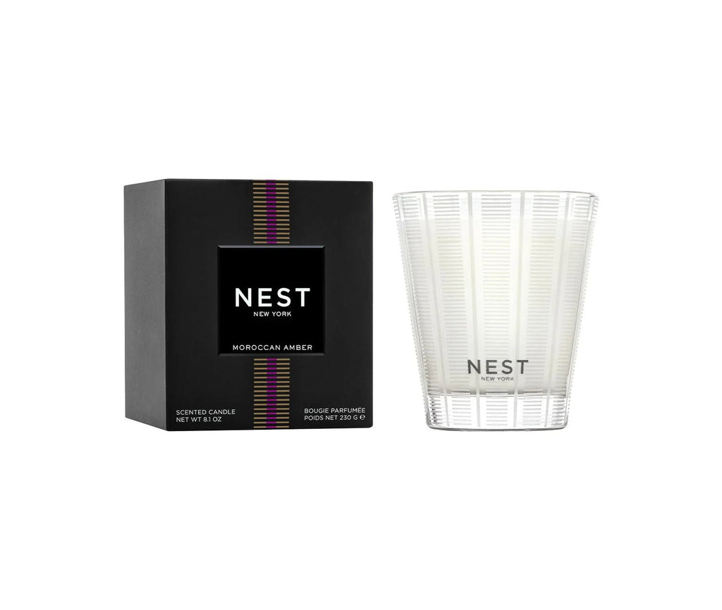 The Nest - Moroccan Amber Classic Candle by Nest features a clean burn in a clear, striped glass jar and comes in a black, rectangular box with colorful vertical stripes and product labeling.