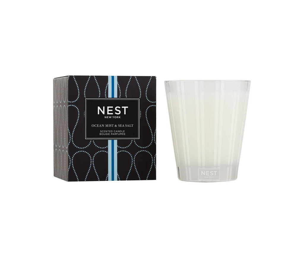 The Nest - Ocean Mist & Sea Salt Classic Candle by Nest comes in a frosted glass holder next to its stylish black and blue box, filling the air with fresh ocean mist and sea salt scents.