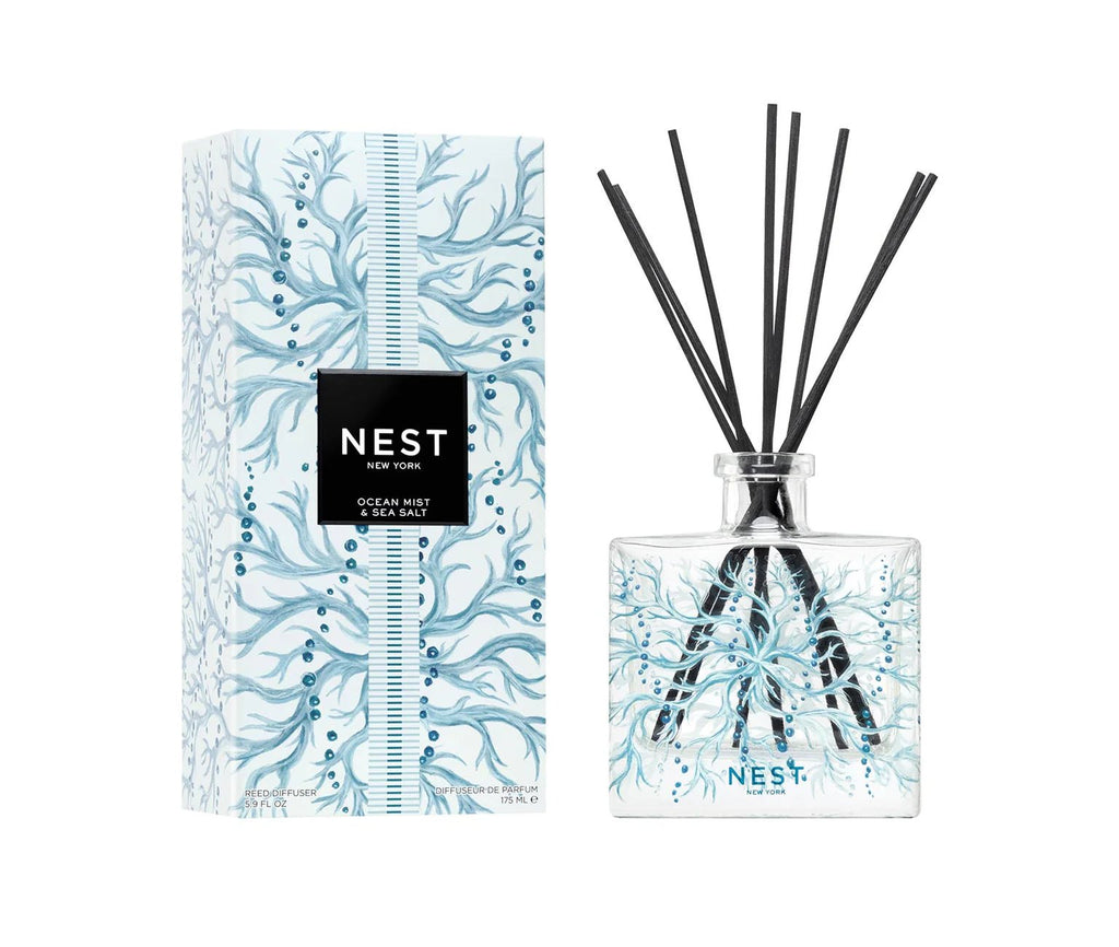 The Nest - Ocean Mist & Sea Salt Decorative Reed Diffuser by Nest features a clear glass bottle with black reeds and a blue seaweed design, presented in a decorated box and filled with refreshing fragrance oils for any space.