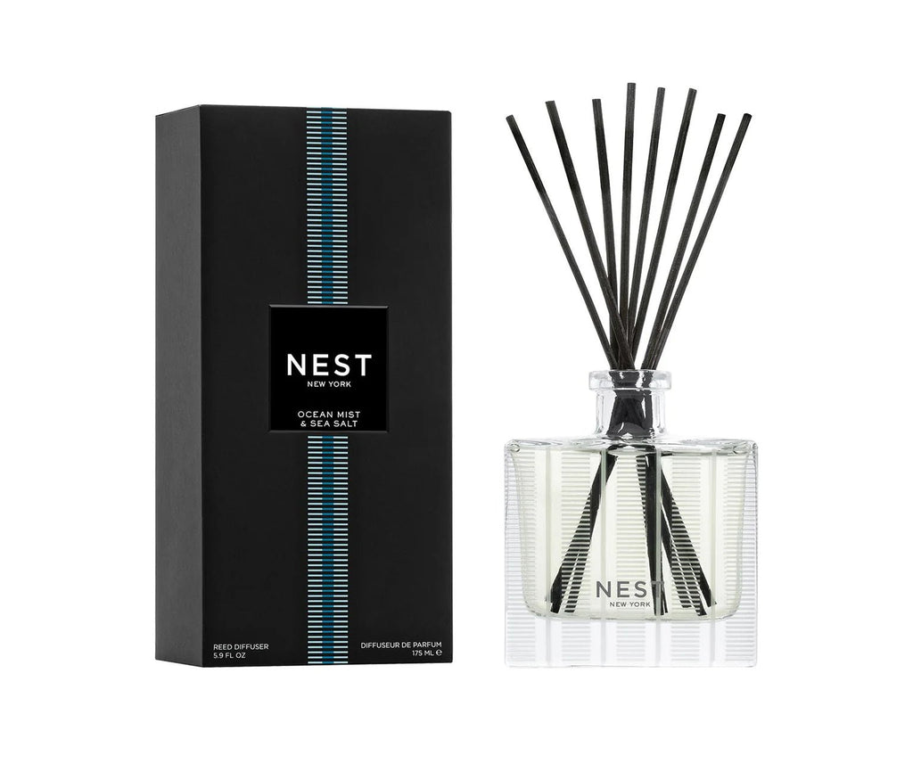 The Nest - Ocean Mist & Sea Salt Reed Diffuser features fragrance oils in a clear glass bottle with black reeds, packaged in a sleek box with blue and white accents for a fresh coastal look.