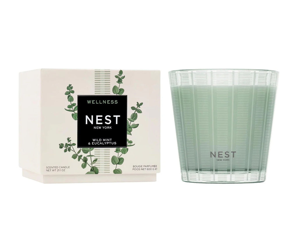 A green glass Nest - Wild Mint & Eucalyptus 3-Wick Candle sits beside its box, featuring the brand name and a eucalyptus-and-basil inspired design.