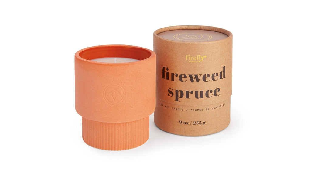 Part of the Sahara Collection, a terracotta-colored ceramic candle holder sits beside a cardboard container labeled Firewood Spruce. The 9 oz soy wax candle inside is crafted by Paddywax and poured in Nashville, embodying warm elegance.