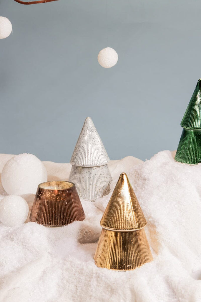 Paddywax 7oz Cypress + Fir Mercury Trees in gold stand on artificial snow, with white foam balls floating above—an enchanting winter display inspired by mercury glass candles.