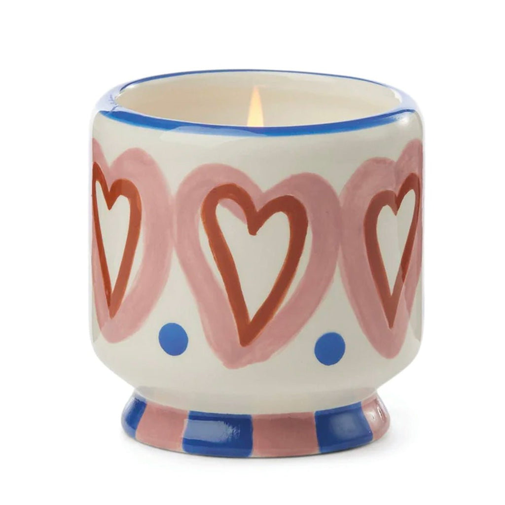 The Paddywax A Dopo 8 oz Handpainted Hearts Ceramic candle features a white holder with pink and red hearts, blue dots, and stripes—perfect for enjoying its bold Rosewood Vanilla fragrance.