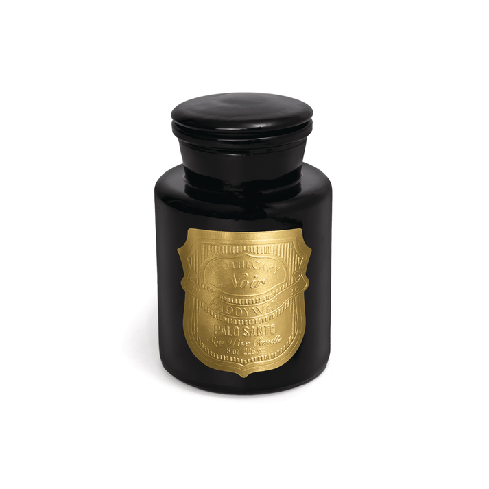 The Paddywax Apothecary Palo Santo 8oz candle features a black glass jar with a rounded lid and a large gold decorative label, all set against a plain white background.