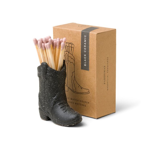 The Paddywax Black Cowboy Boot Match Holder, crafted from black ceramic, exudes rustic charm and comes in a Black Ceramic labeled brown box. Ideal as a Nashville gift, it combines style with practicality, featuring matches with vibrant pink heads.