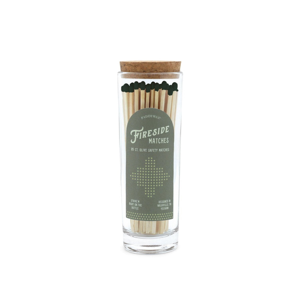 The Paddywax - Fireside Safety Matches feature long wooden matches with green tips in a clear glass jar sealed by a cork. The label, Fireside Matches, is styled with decorative text and trees, providing a vintage look as a perfect candle companion.