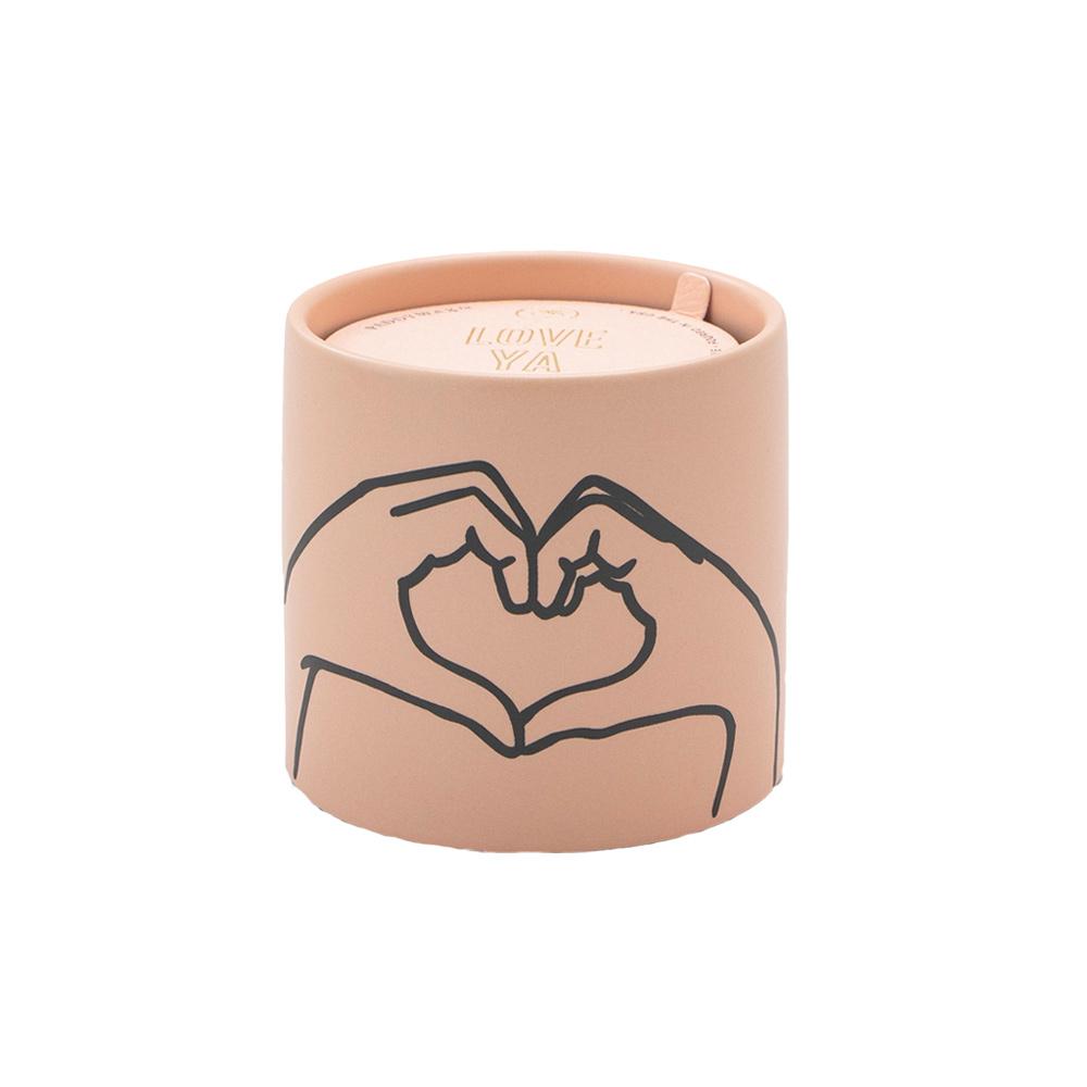 The Paddywax Impressions candle is a beige ceramic cylinder with an exterior design of hands forming a heart. It features a colorful matte lid inscribed with LOVE YA and is fragranced with warm tobacco and vanilla.