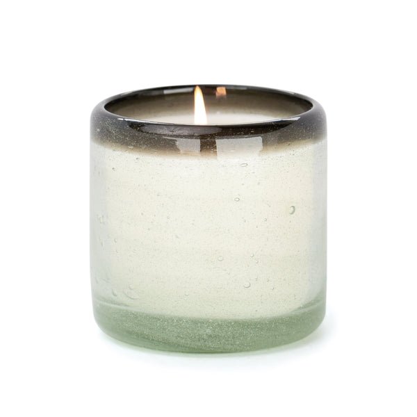 The Paddywax - La Playa - Vanilla Rosa 9oz Candle is housed in a translucent, hand-blown bubble glass holder with a dark-to-light gradient. The lit candle emits a bright, steady flame that casts a warm glow through its smooth, rounded form.