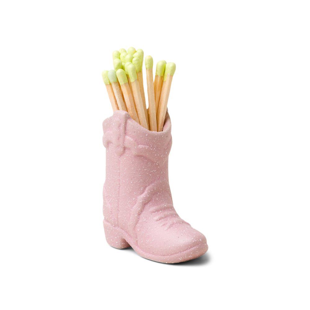 The Paddywax Pink Cowboy Boot Match Holder by Paddywax offers a Western flair, cradling wooden matches with light green tips neatly arranged upright, enhancing this vintage-inspired piece.