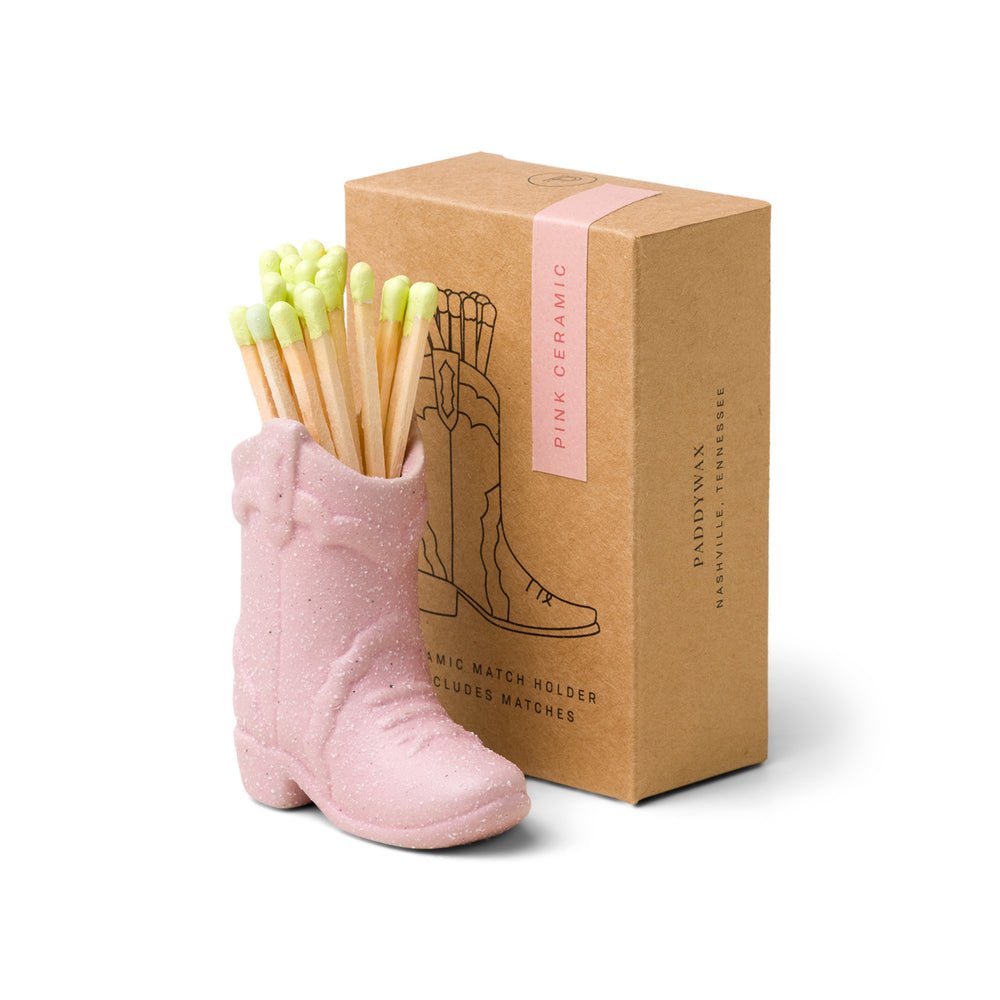 The Paddywax - Pink Cowboy Boot Match Holder is a vintage-inspired ceramic holder filled with matches. It adds a Western vibe to your decor and is packaged in a cardboard box labeled Pink Ceramic, complete with an illustration of the charming boot-shaped holder, by Paddywax.