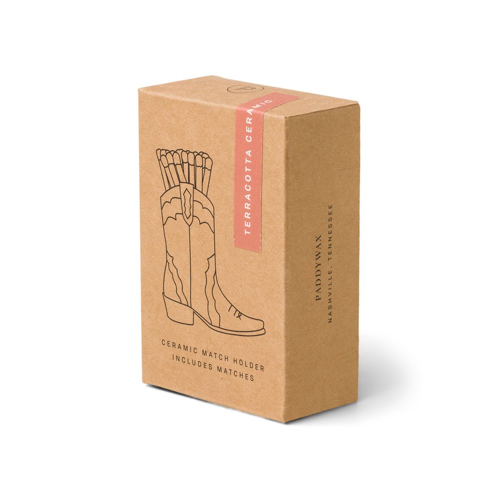 A brown box featuring a line drawing of a ceramic cowboy boot filled with matches includes text: Terracotta Ceramic Match Holder Includes Matches. The brand name Paddywax is elegantly shown, making it an ideal Nashville gift.