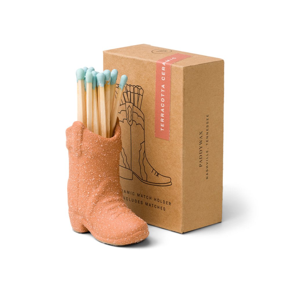 The Paddywax Terracotta Cowboy Boot Matches set features a terracotta boot-shaped holder with blue-tipped matches, alongside a brown box illustrated with the boot. Its an ideal Nashville gift.