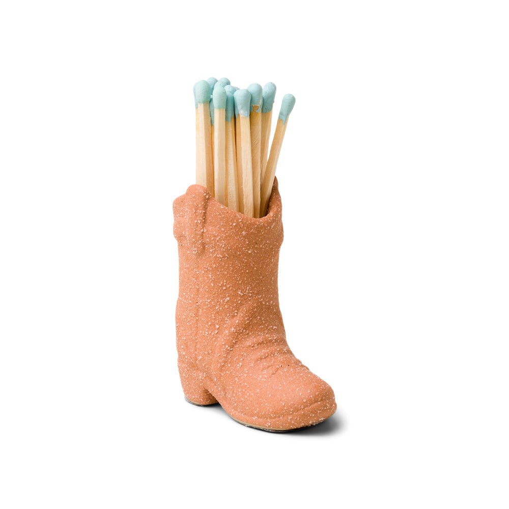 The Paddywax Terracotta Cowboy Boot Matches, a Nashville gift from the brand Paddywax, features intricate details and stands on a plain white background while holding several wooden matches with striking blue tips.