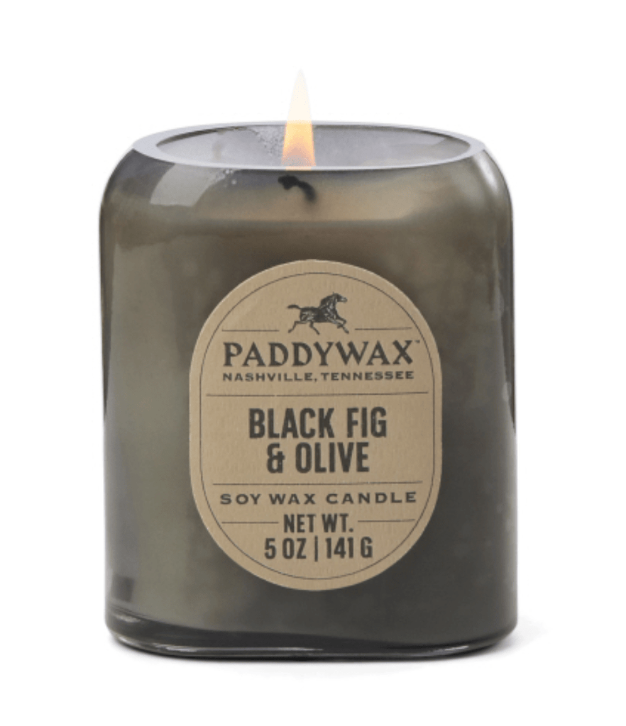 A small, steady flame flickers in the dark glass jar of the vintage-inspired Paddywax Vista Black Fig & Olive Soy Wax Candle, Nashville, Tennessee. It weighs 5 oz (141 g).