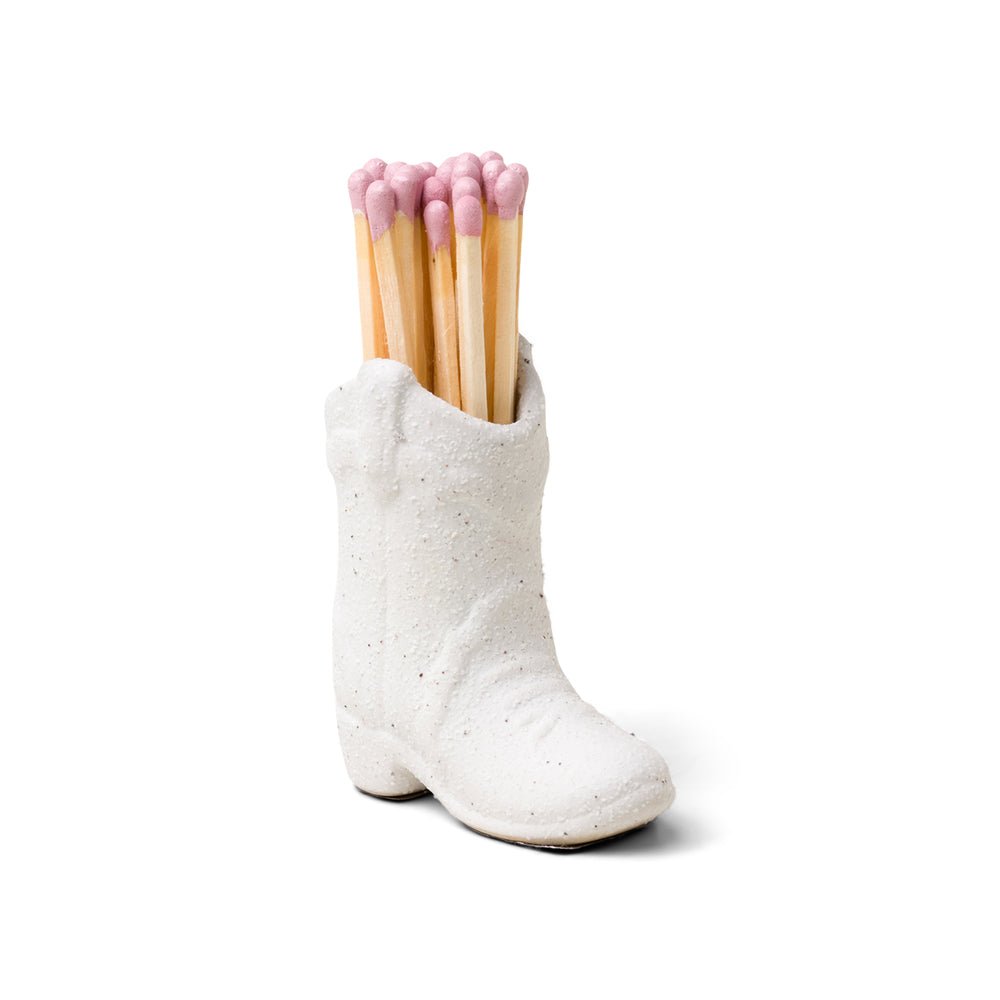 The Paddywax White Cowboy Boot Match Holder is a vintage-inspired ceramic piece that holds long matches with light pink tips.