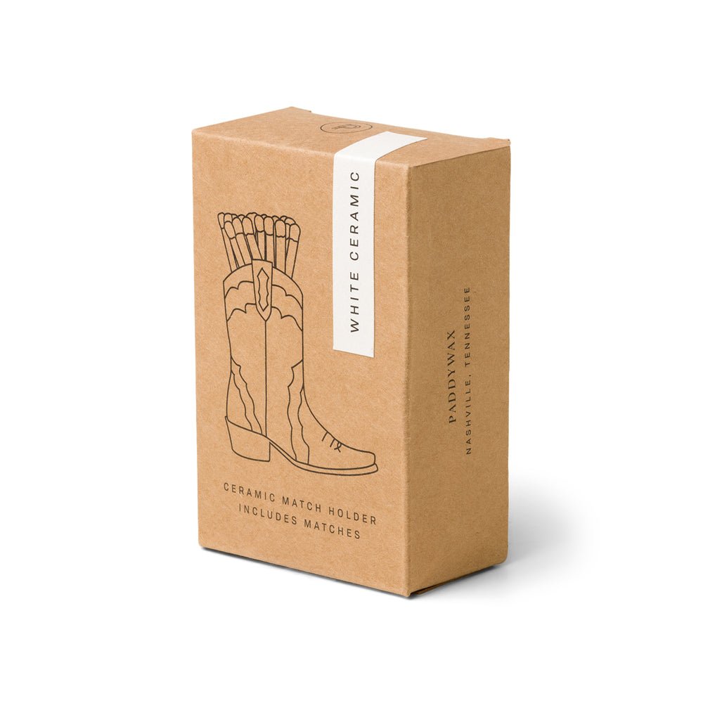 The packaging features the Paddywax White Cowboy Boot Match Holder, adorned with a line drawing of a cowboy boot filled with matches. This ceramic accessory exudes a charming Western vibe and includes matches.