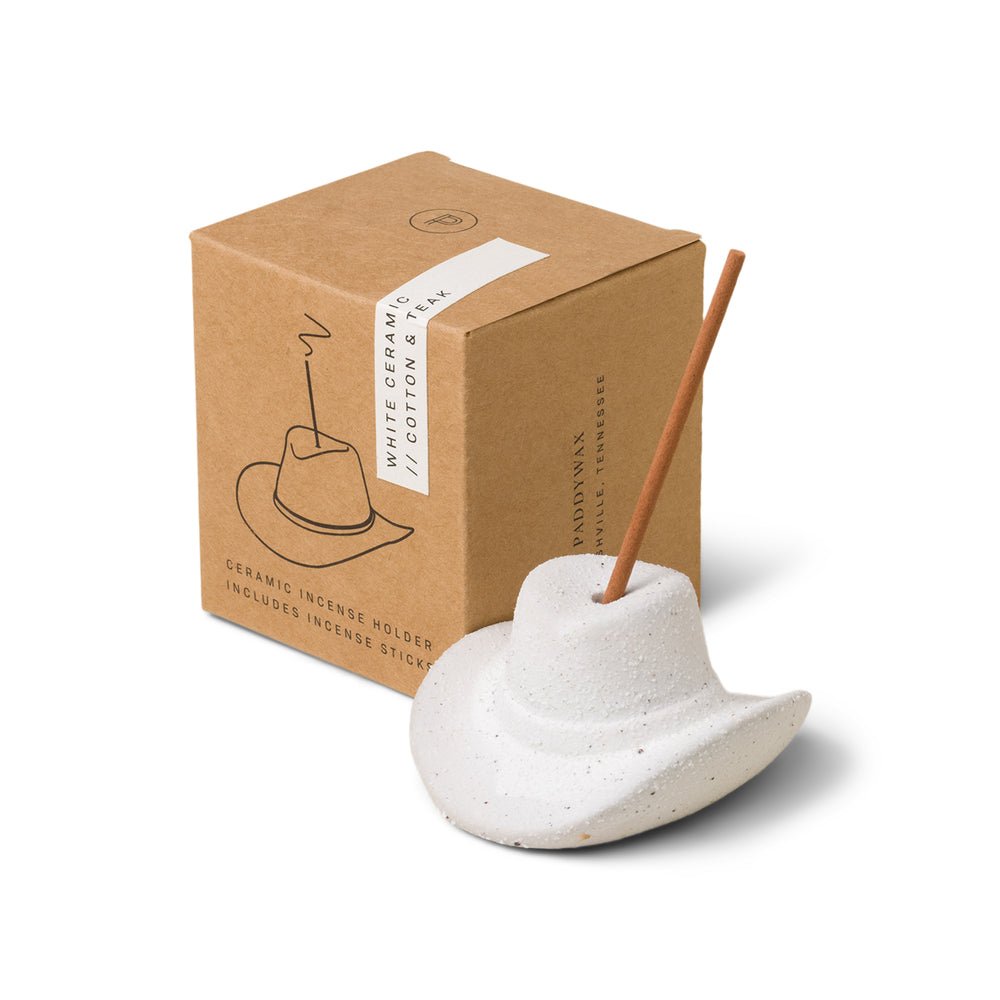 The Paddywax White Cowboy Hat Ceramic Incense Holder stylishly cradles an incense stick, beautifully pairing with a brown box featuring the hat illustration and product details.