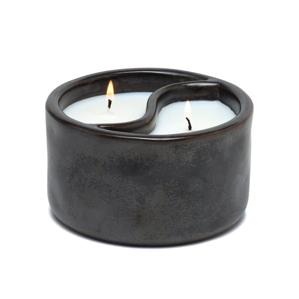 The Paddywax Yin-Yang Palo Santo + Cade candle features a round black ceramic holder with a yin-yang design, including two candles. One burns, releasing calming scents to cultivate peace, while the other remains unlit. The matte finish adds a smooth touch to the experience.