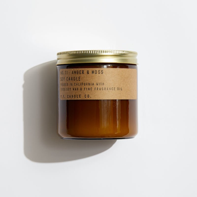 The P.F. Candle Co. - 12.5 oz. Amber Moss Candle in a brown glass jar with a gold lid provides a fresh earthy aroma using 100% soy wax and fine fragrance oil, offering a strong scent throw. Made by P.F. Candle Co., its crafted in California for delightful ambiance enhancement.