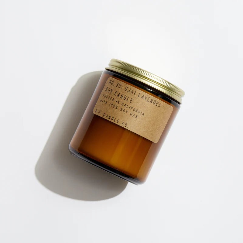 The P.F. Candle Co. 7.2 oz. Ojai Lavender Candle features a brown glass jar with a gold lid and beige label reading No. 35: Ojai Lavender. This soy candle offers a fresh, earthy scent, embodying Californian origins while casting a soothing shadow on any surface for tranquility and calmness.