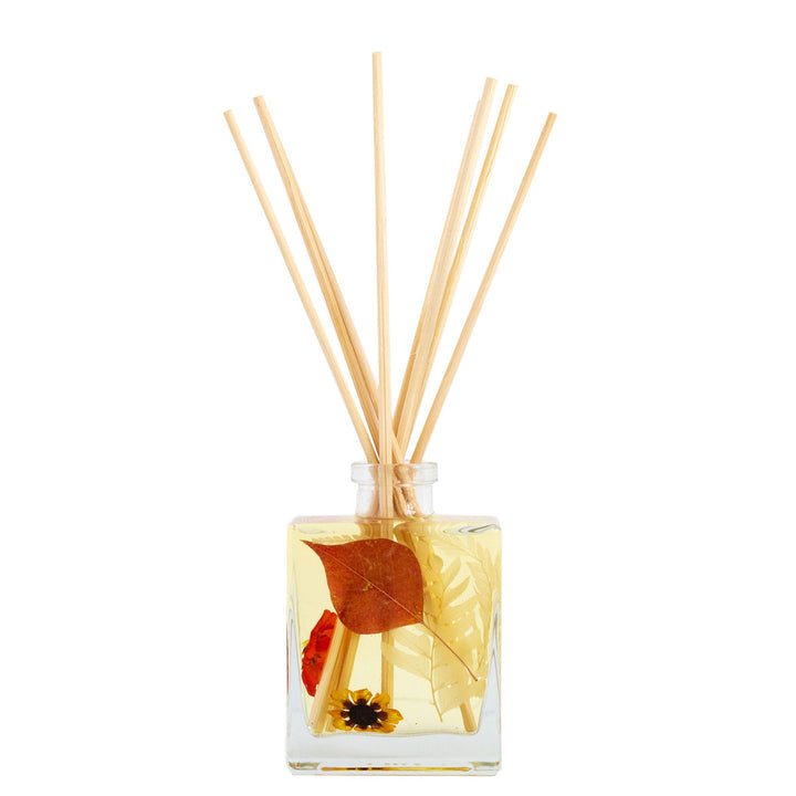 The Rosy Rings Botanical Diffuser - Honey Tobacco 4oz showcases several reed sticks from the top, with the glass bottle containing transparent liquid enriched with decorative natural elements like dried leaves and small seeds to enhance its fragrance.