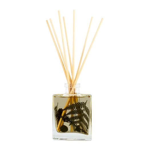 The Rosy Rings - Forest 4oz Botanical Diffuser features a square glass bottle with liquid and green fern leaves, accented by wooden reeds that diffuse a botanical fragrance. The image shows this elegant diffuser against a pristine white background.