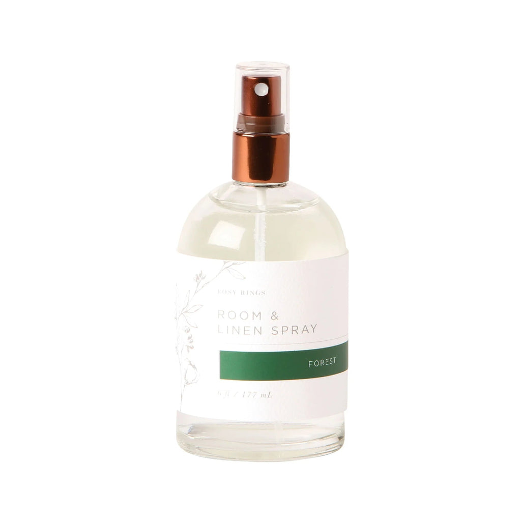 A clear 6 fl. oz. Rosy Rings room and linen spray bottle with a brown nozzle features the Forest label adorned with floral graphics, suggesting cedarwood and pine scents.