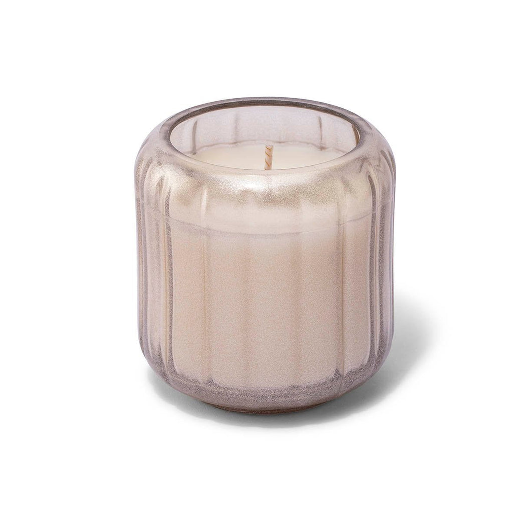 The Skeem Champagne Candlescape 8 oz Candle in Yuzu Pine features a round, textured glass holder with a frosted light beige appearance and subtle vertical grooves. It contains a white candle with a visible wick, casting soft shadows on its plain white background.